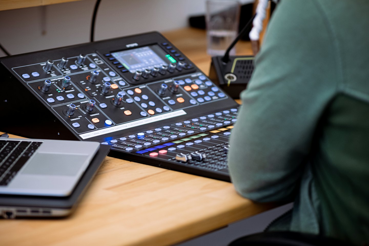 Profesional ajustando mesa de mezclas de audio junto a un portátil.