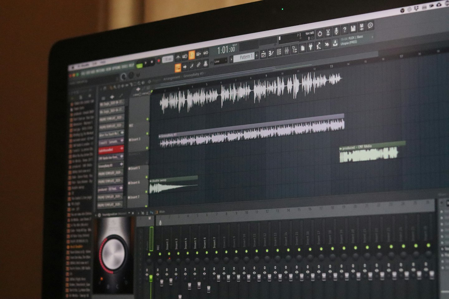 Pantalla de portátil mostrando software de producción musical con formas de onda y deslizadores.